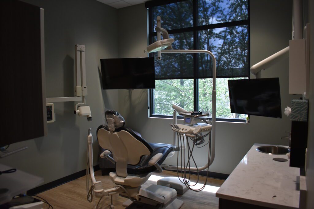A dentist 's office with two monitors and three chairs.